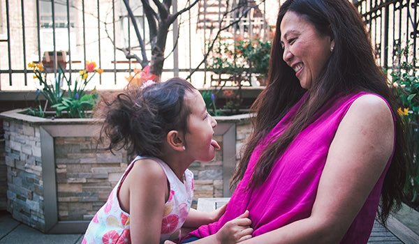 A mother and daughter are smiling at each other in a picture outside of the Ronald McDonald House New York. The daughter sticks ehr tongue out at the mother in a playful way.