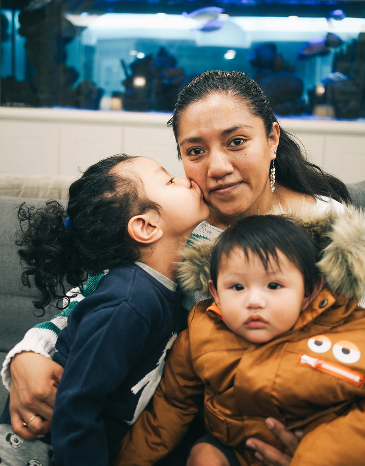 A child undergoing cancer treatment at a local hospital kisses his mom on cheek and his little brother is sitting close on his mom's lap