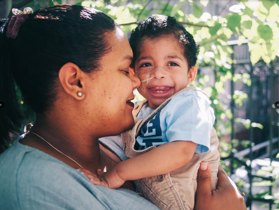 A caregiver mother holds her two year old son as he smiles and laughs at Ronald McDonald House New York