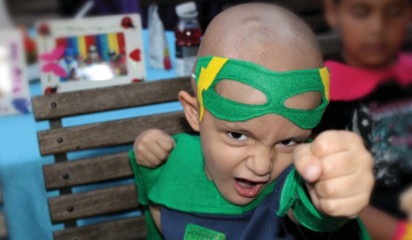 A young child dressed in a green super hero costume makes a pose with their fists. The child poses for the camera.