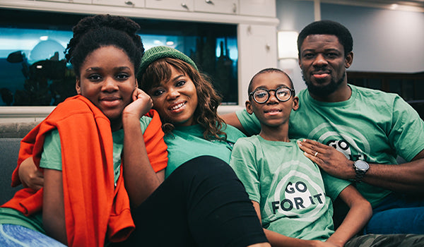 From left to right: A daughter, mother, son and father sit on a couch in the Ronald McDonald House New York. They are all smiling at the camera for a picture.