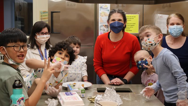 Programs manager and cooking class teacher with class of kids in kitchen at RMH-NY
